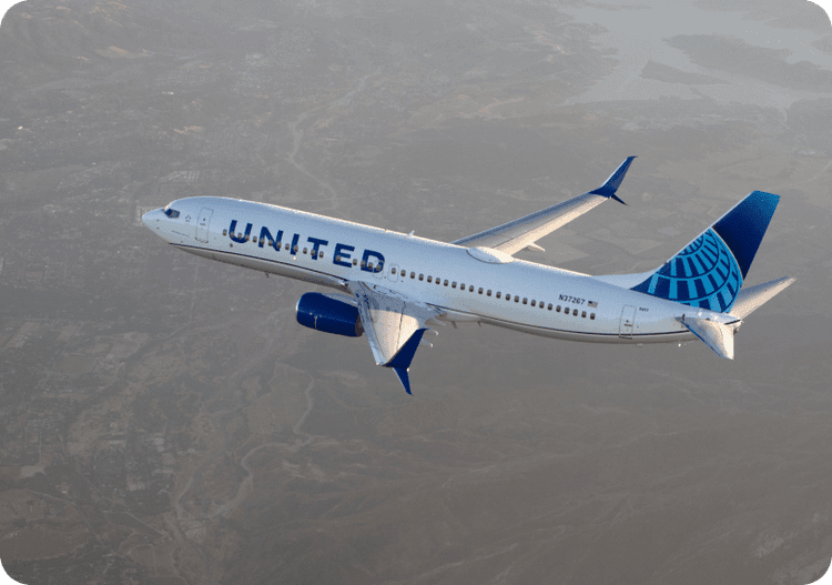 United Airlines airplane flying over mountainous landscape with cloudy sky