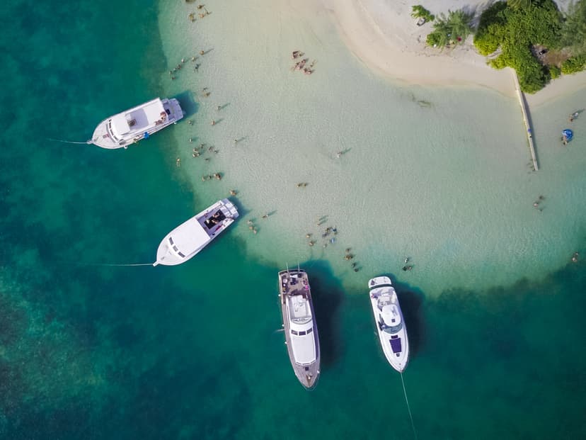 An aerial photo of a beach with 4, 30 foot yachts anchored very close to shore.