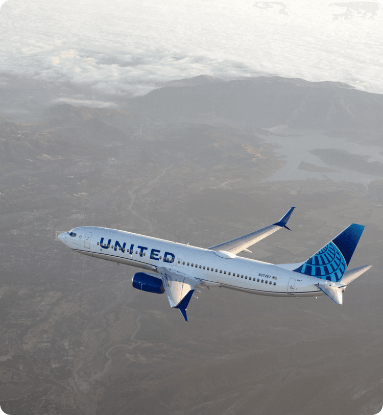United Airlines airplane flying over mountainous landscape with cloudy sky