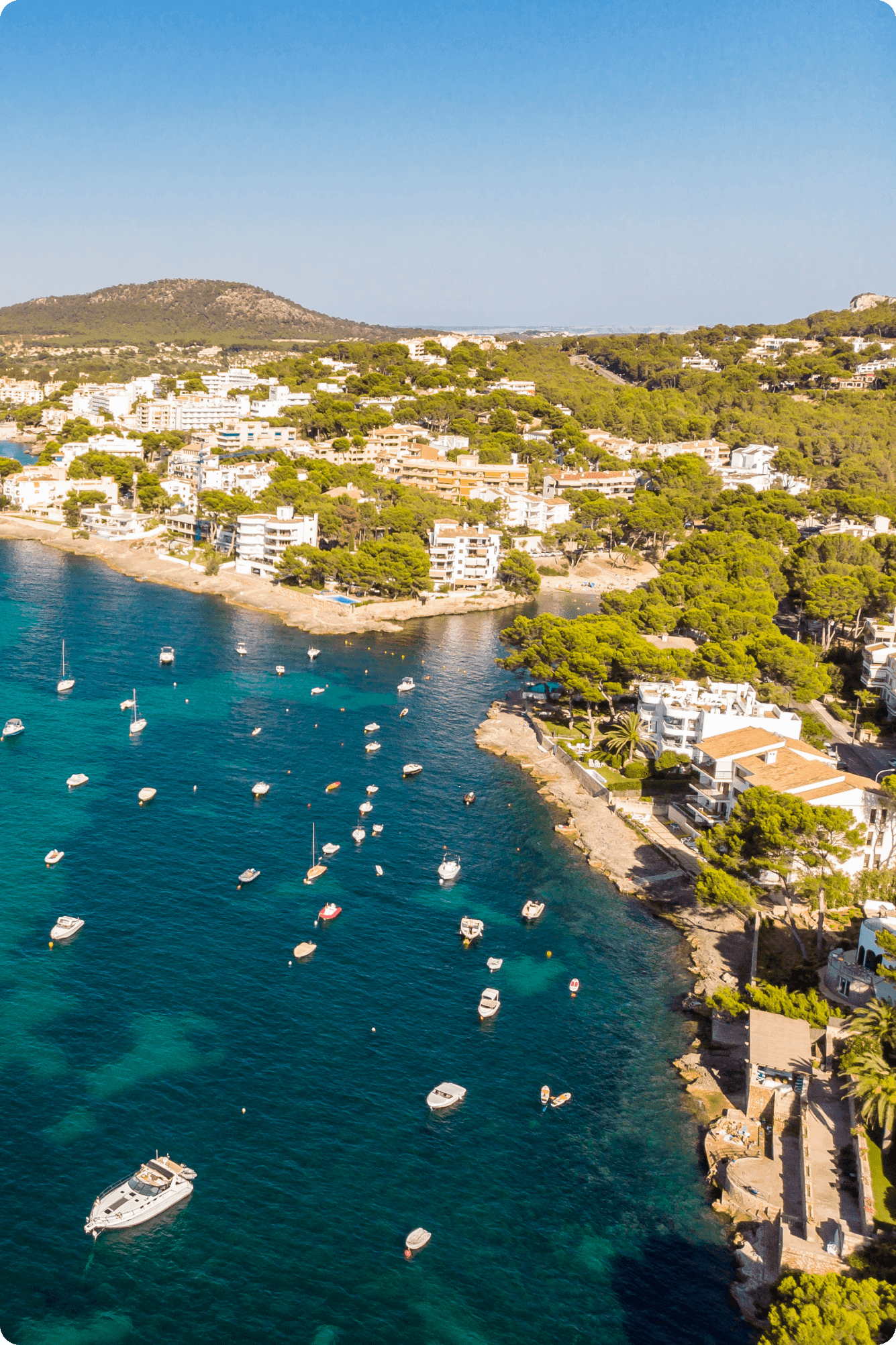 Aerial view of a scenic coastal bay with numerous boats anchored in crystal clear turquoise waters
