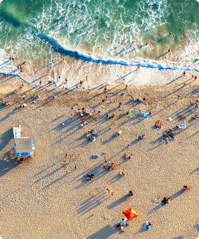 Aerial view of a crowded beach with people near shoreline and waves rolling in.