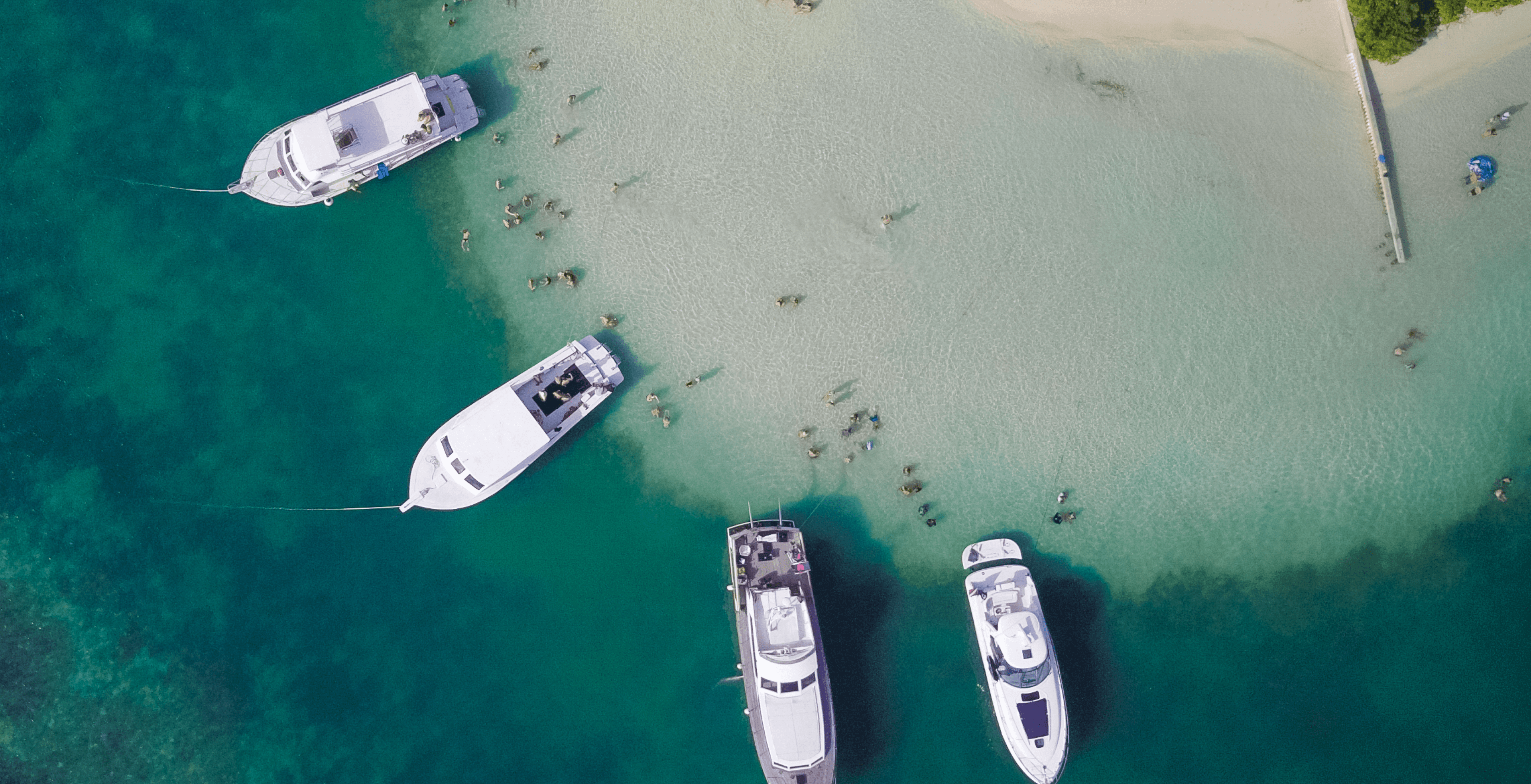 An aerial photo of a beach with 4, 30 foot yachts anchored very close to shore.