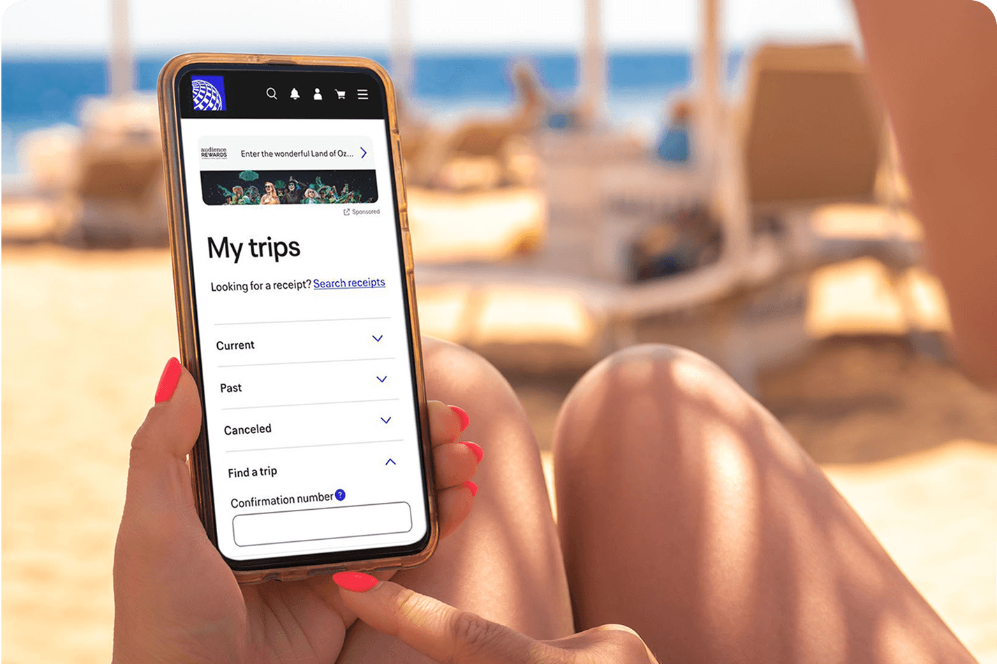 Traveler holding a phone showing a trip app while relaxing on a sunny beach.