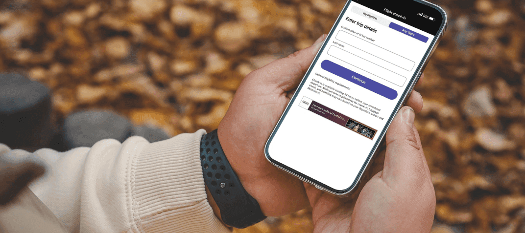 A person sitting on a bench in the fall with leaves on the ground viewing the United mobile app screen.