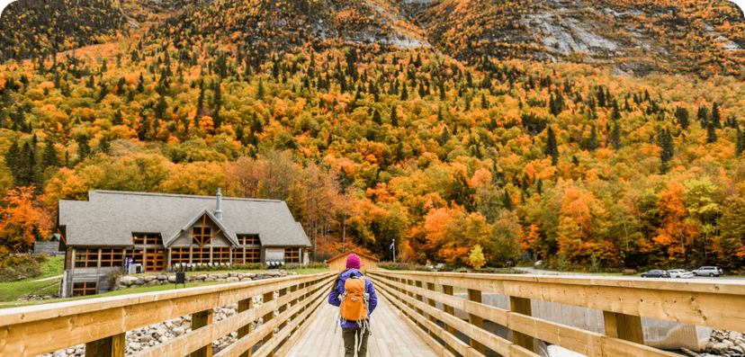 Person walking across a wooden bridge with a fall forest in the far distance
