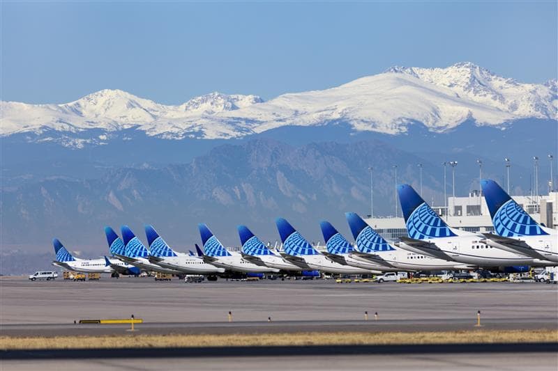 A row of United Airline planes parked at their airport terminals with snow capped mountains in the background
