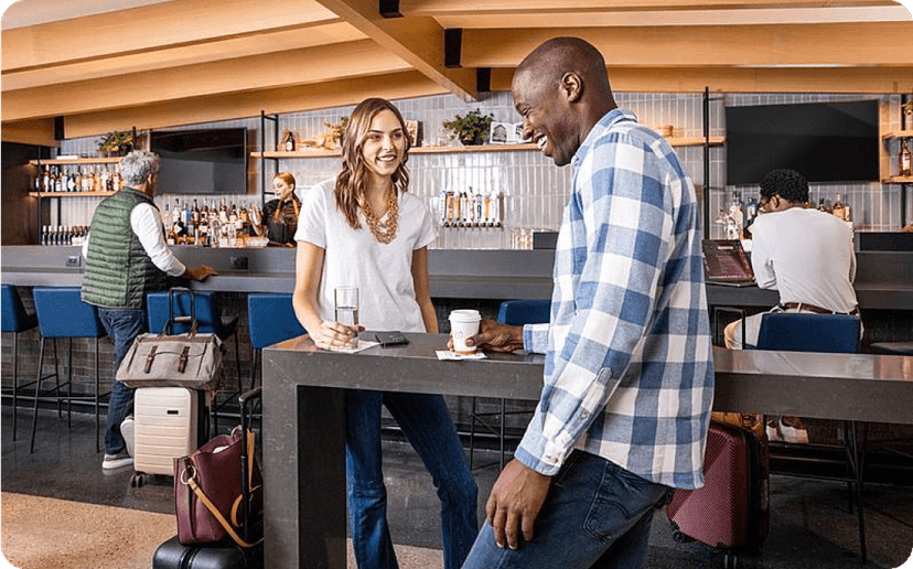 Two travelers drinking and talking in an airport club.