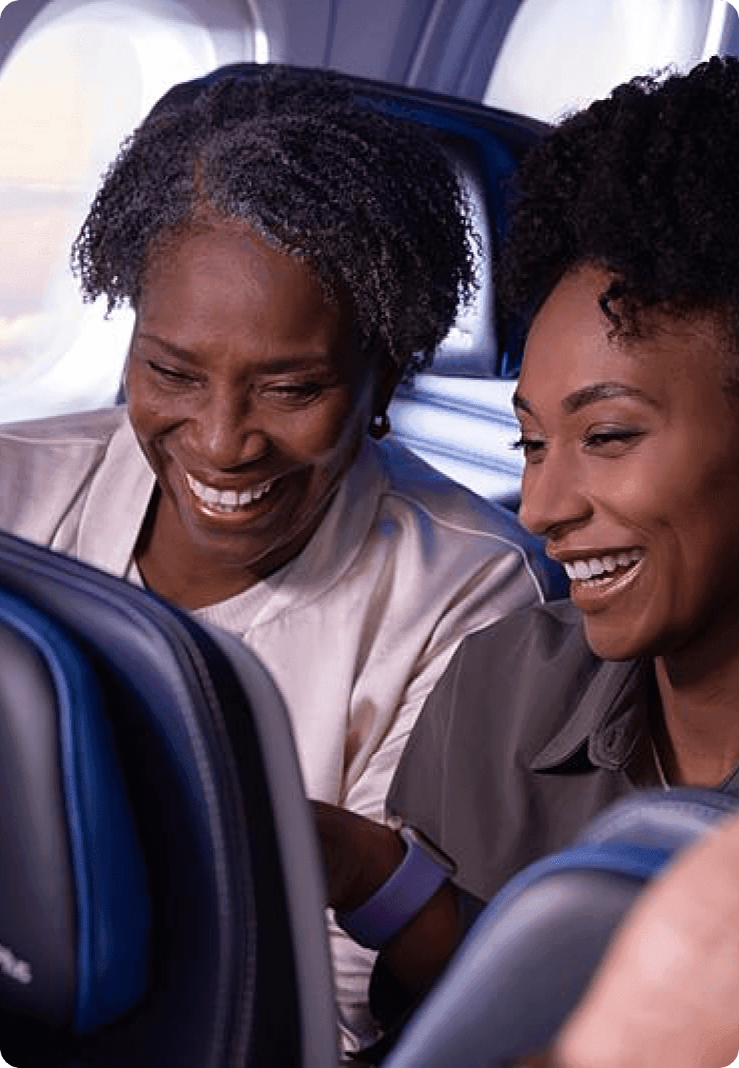 Two travelers smiling at a inflight entertainment screen on their plane.