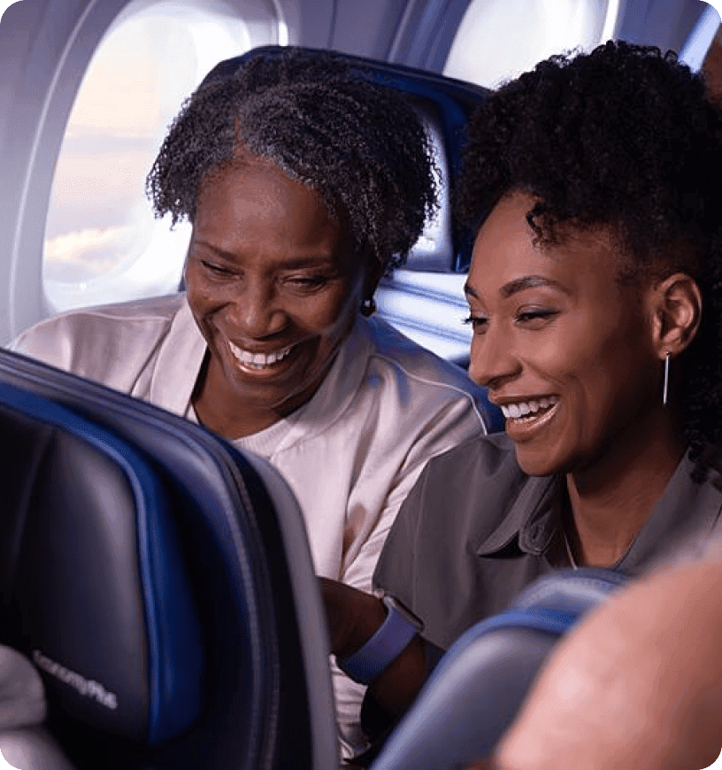 Two travelers smiling at a inflight entertainment screen on their plane.