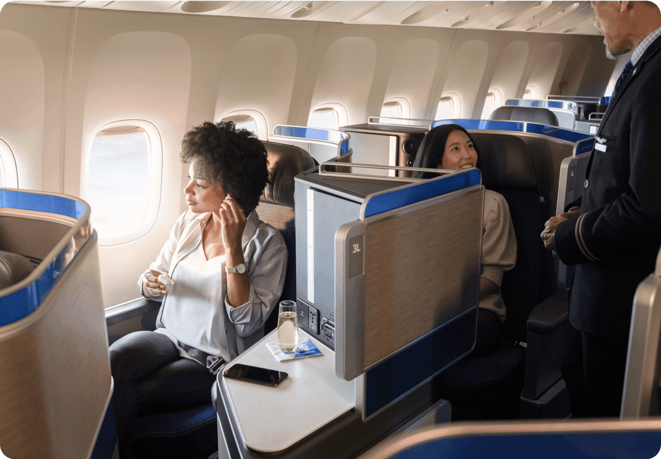 Two travelers in business class seats on a plane relaxing and talking to a flight attendant