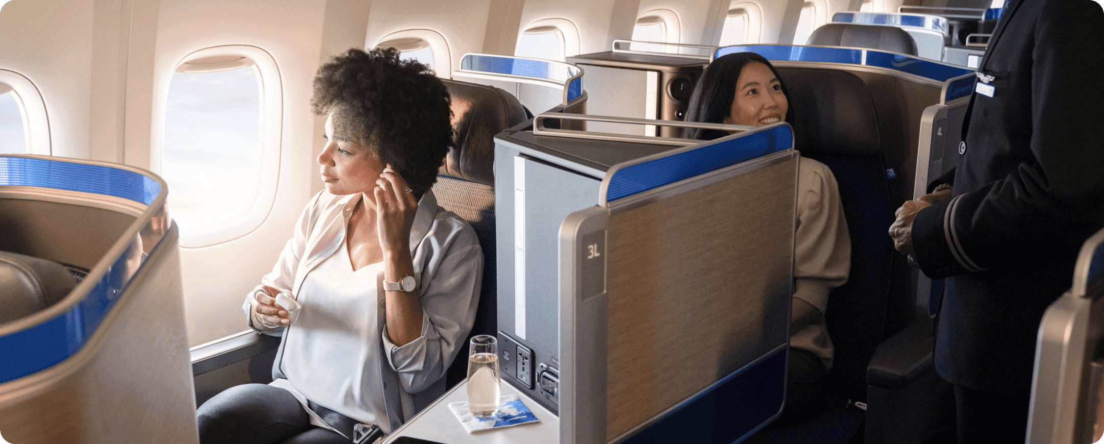 Two travelers in business class seats on a plane relaxing and talking to a flight attendant