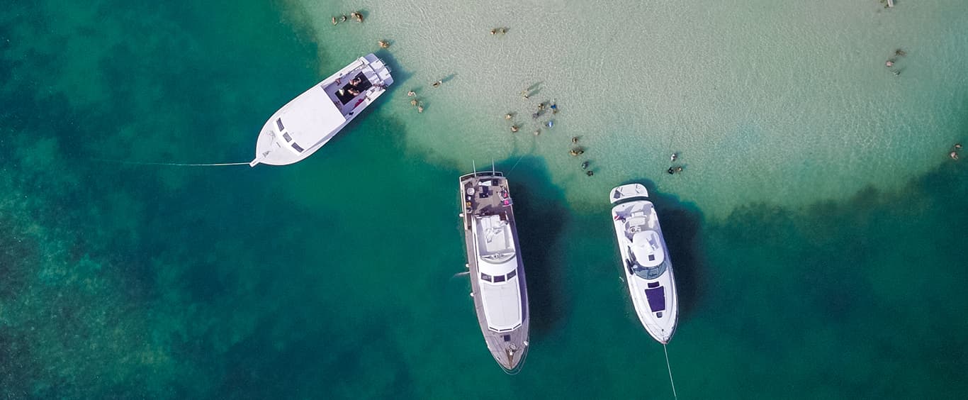 An aerial photo of a beach with 4, 30 foot yachts anchored very close to shore.