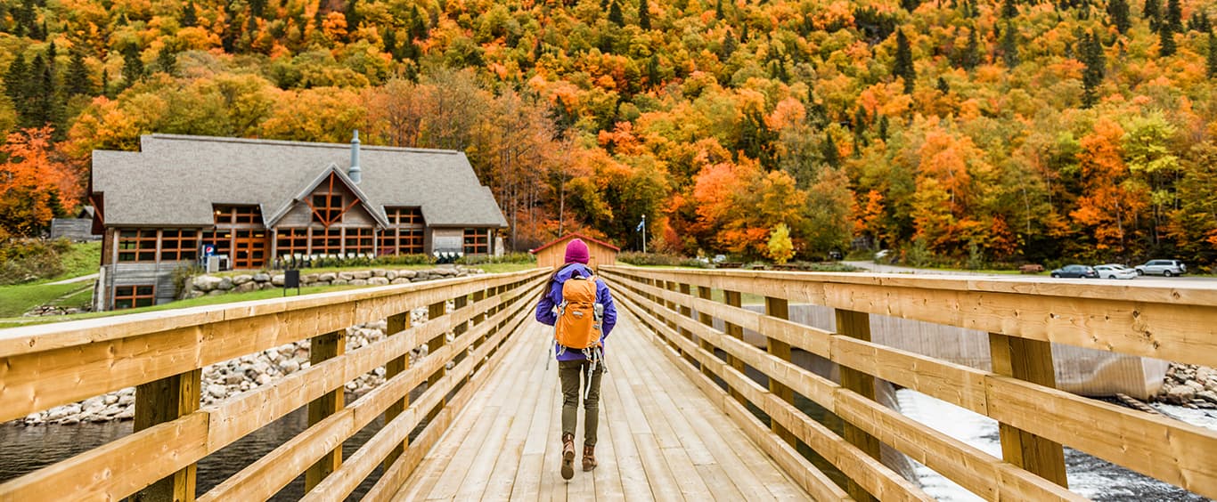 Person walking across a wooden bridge with a fall forest in the far distance