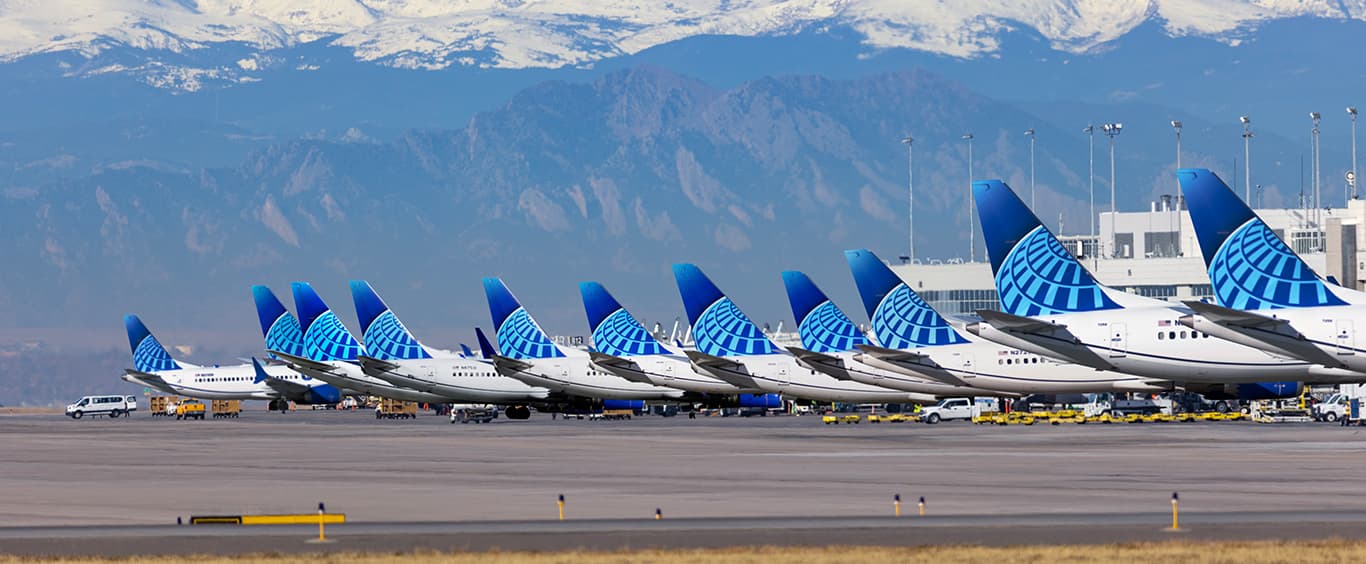 A row of United Airline planes parked at their airport terminals with snow capped mountains in the background